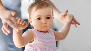 Liten flicka lär sig gå med hjälp av sin mamma.