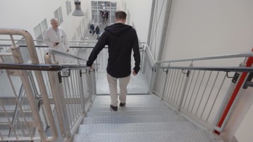 Överläkaren i neurologi och professorn Peter Andersen observerar sin ALS-patient som går ned för en av trapporna på Norrlands universitetssjukhus.