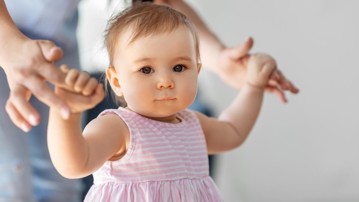 Liten flicka lär sig gå med hjälp av sin mamma.