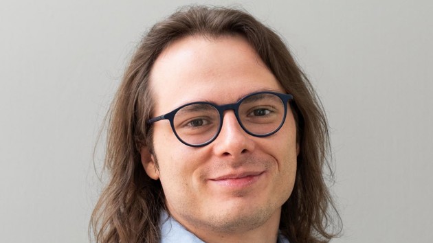 A man with long hair wearing glasses and a blue shirt. 