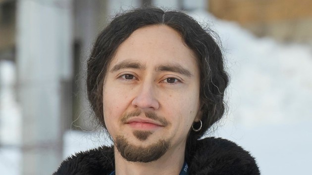 A man standing in front of a building wearing a black jacket.