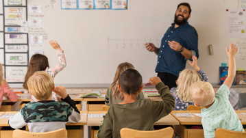 Barn i klassrum räcker upp handen.