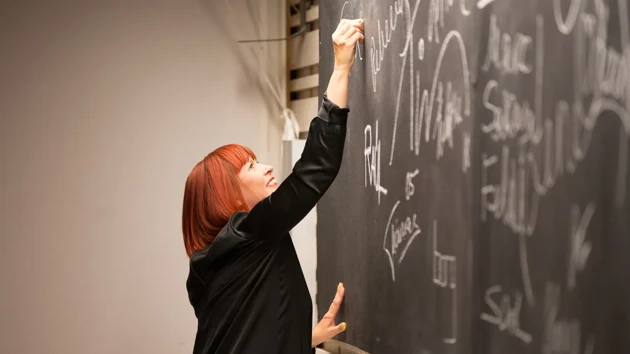 Woman signing a black board with a white chalk