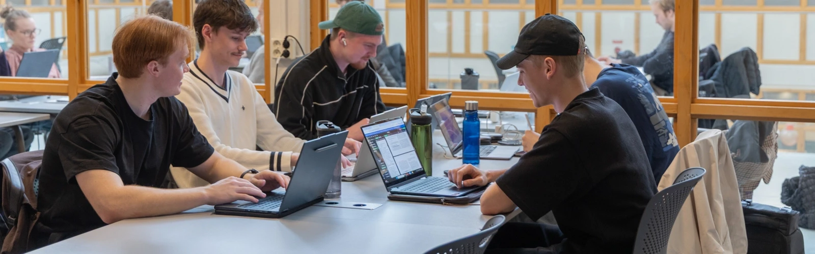 En grupp studenter sitter vid ett bord med bärbara datorer.