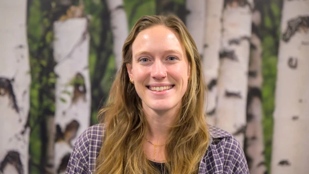 A woman smiling poses in front of a birch tree background
