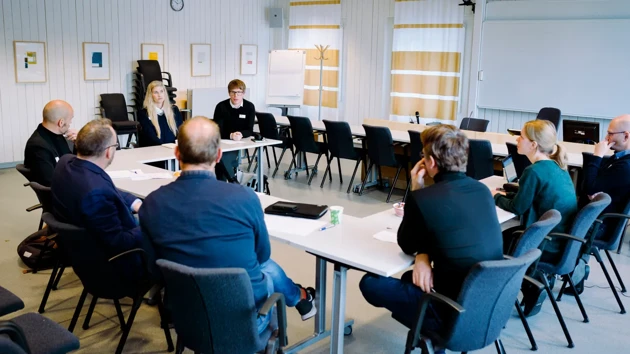Eight people sat at a table formation facing each other in a conference room.