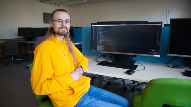 Foto på Algot Heimerson sittande i datorsal, skärmar i bakgrunden