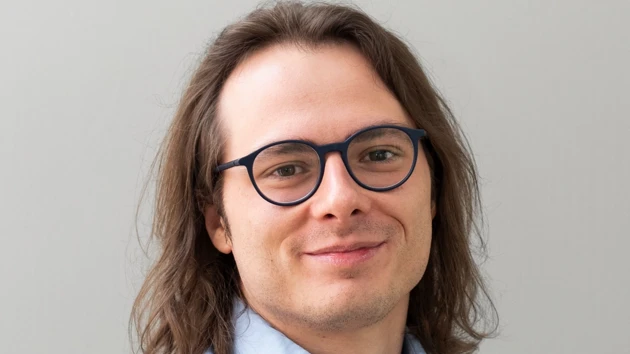 A man with long hair wearing glasses and a blue shirt.