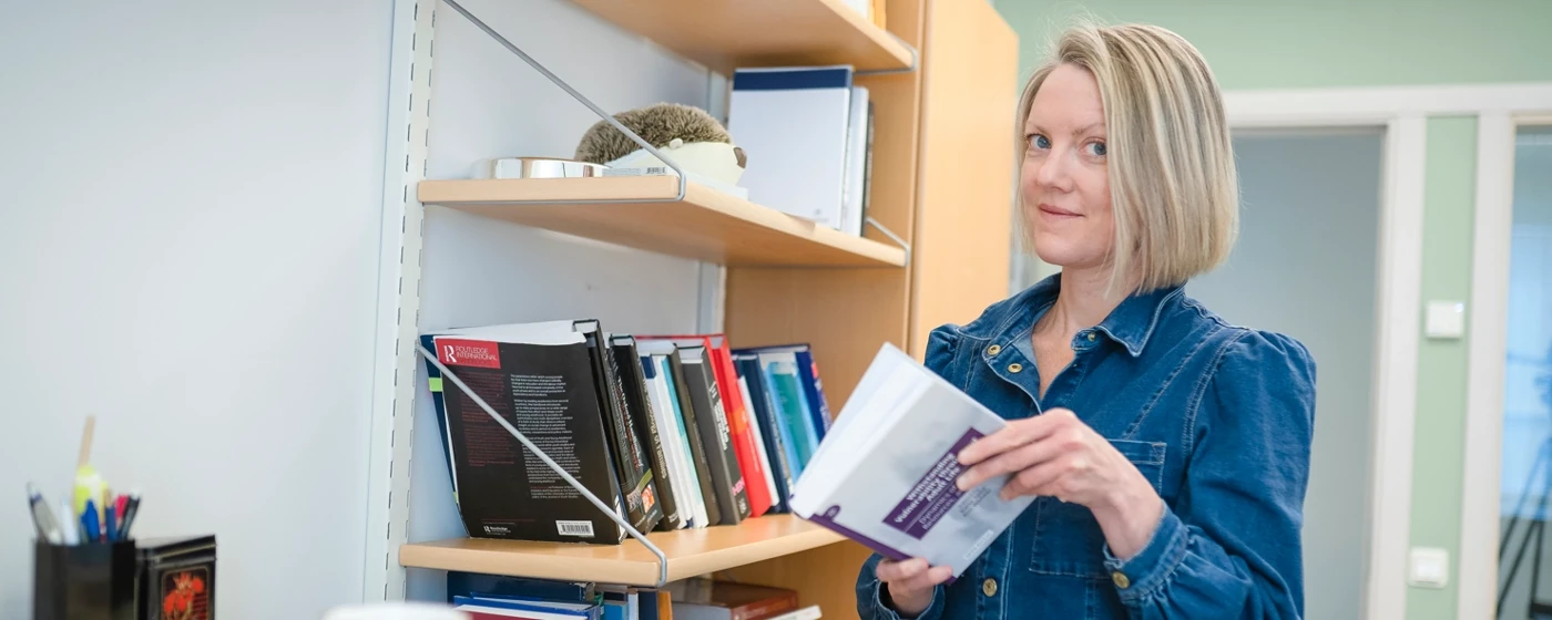 En kvinna står vid en bokhylla i ett kontor och bläddrar i en bok.