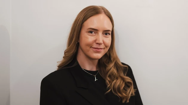 Chelsie Svensson i svart kavaj står framför en vit vägg.