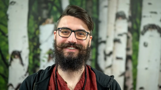 En man med skägg och glasögon framför en björk tapetbakgrund