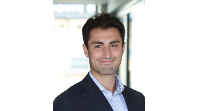 Daniel Ghazi i kostym ler mot kameran.