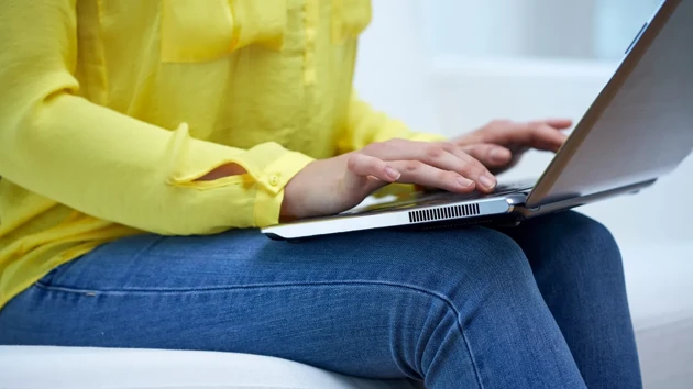 A person is sat typing on a laptop on her lap.