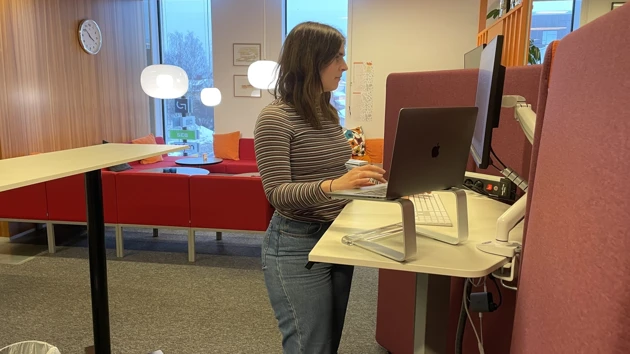 Photo of Elin Lindén standing i front of the computer at her desk