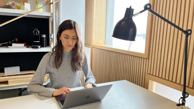 Bild på Emma Biondani, sitter vid sitt skrivbord på Arkitekthögskolan och skriver på sin laptop.