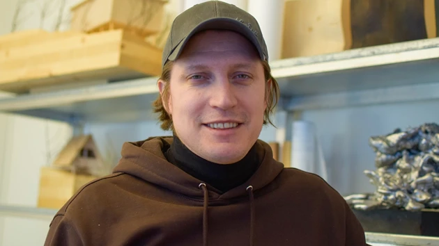 Bild på Erik Karlsson stående framför hylla med föremål av trä och metall