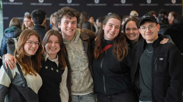 Smiling students holding each other over the shoulders in a row.
