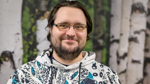 Ett huvud- och axelporträtt av Florian Albrecht som bär en vit huvtröja med marina motiv, mot en bakgrund av vit björkskogstapet