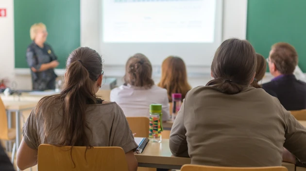 Föreläsningssal på universitet med studenter i förgrunden och en lärare vid tavlan.
