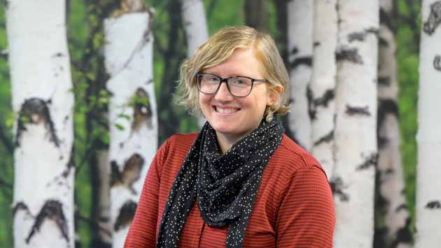 A woman standing in front of a painting of trees