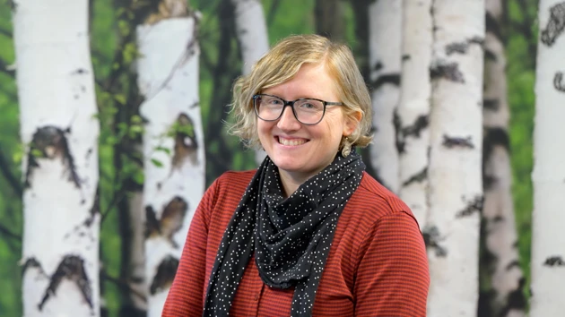 En kvinna står framför en målning med träd