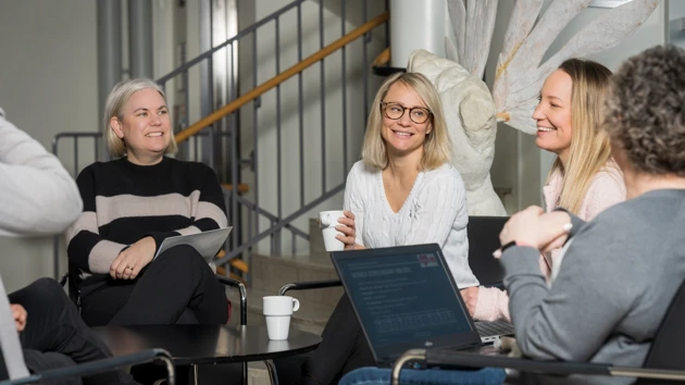 Four women are sat in a circle talking and working.