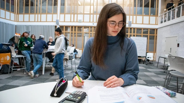 Bild på Hanna Berggren som sitter vid ett bord och löser matematikuppgifter