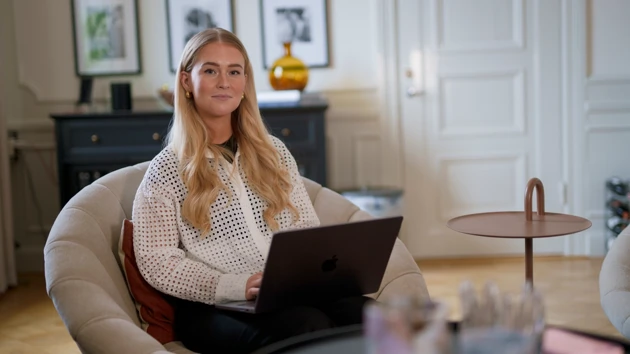 Kvinna sitter i en fåtölj med en laptop i famnen.
