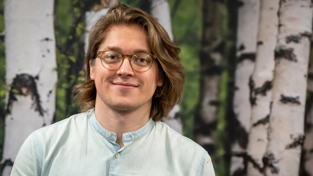 En man med glasögon står framför en målning