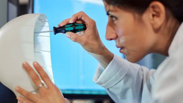 A woman is screwing in a robot-like construction with a screwdriver.
