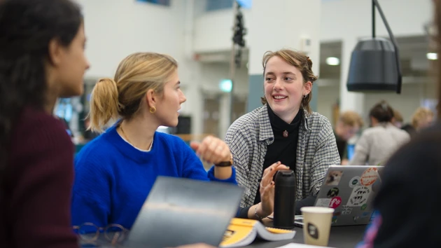 Tre studenter samtalar vid sina datorer.