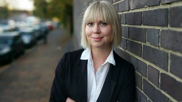 Porträttbild på Jennifer Eriksson, mörk tegelvägg och gata i bakgrunden