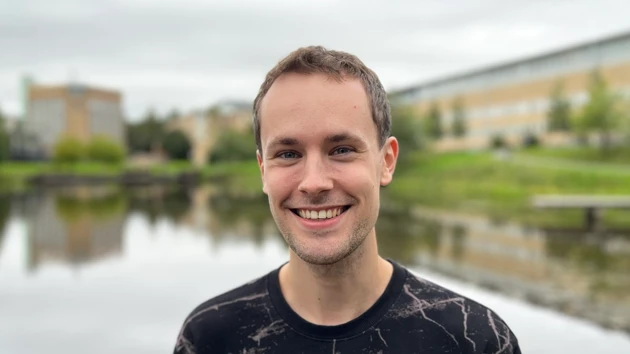 A male student with a broad smile in front of the Campus Pond.