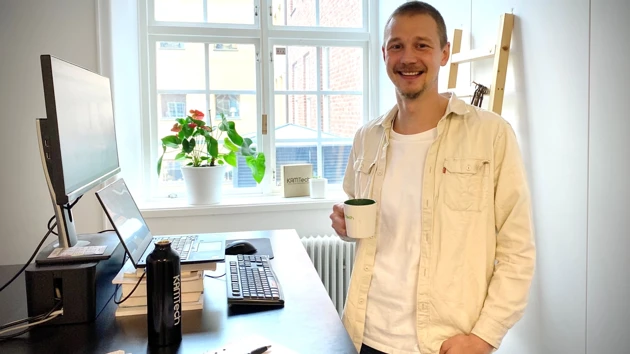 Bild på Kalle Almstedt stående i sitt arbetsrum på Kamtech med en kaffekopp i handen