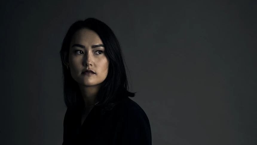 A woman standing in a dark room with her hands in her pockets.