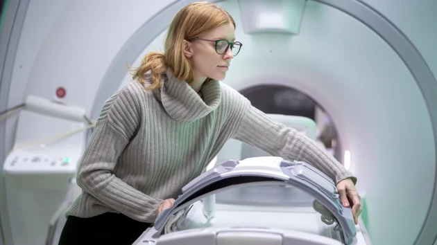 A woman is adjusting a detail on an MRI patient table.