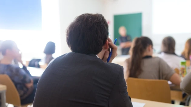En grupp människor som sitter vid bänkar i ett klassrum.