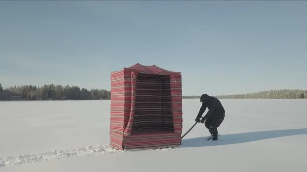 Person som drar en beduintält-liknande släde över snötäckt sjö.