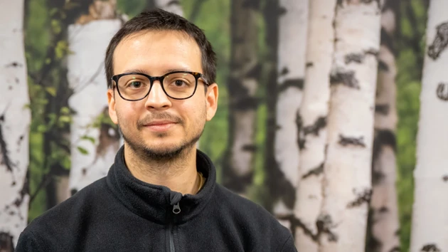 En man med glasögon står framför en målning av träd