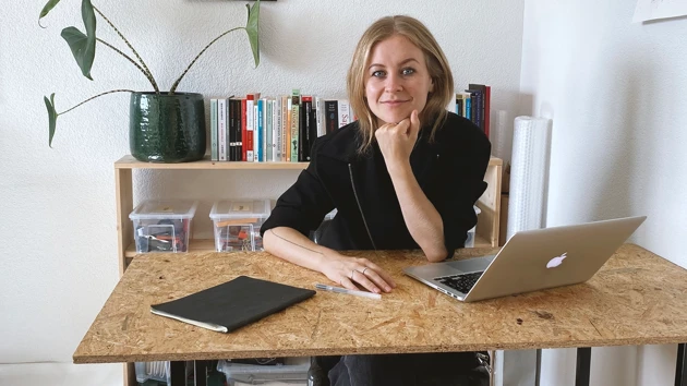 Bild på Maja Malmcrona sittande vid skrivbordet, laptop och anteckningsblock framför henne