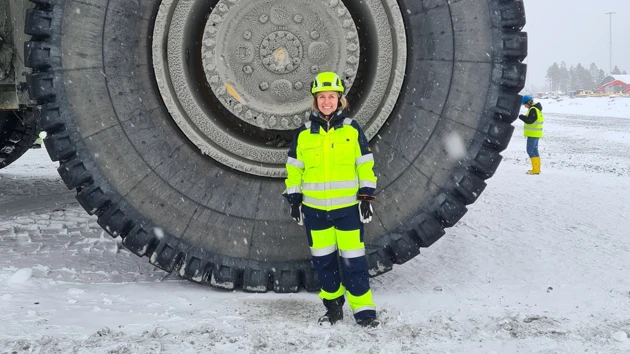 Bild på Malin Suup i reflexkläder och skyddshjälm framför hjulet till en stor gruvmaskin