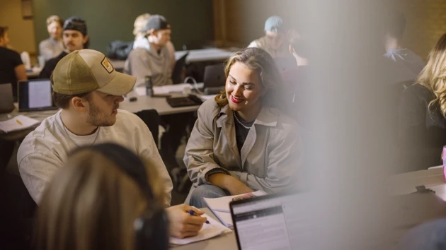 Två leende studenter som sitter vid ett utomhusbord på campus.