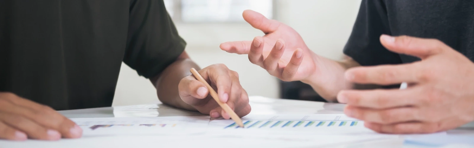 Detalj på två personer som sitter vid ett bord med papper och pratar med varandra. För att illustrera samarbete, möte eller grupparbete.