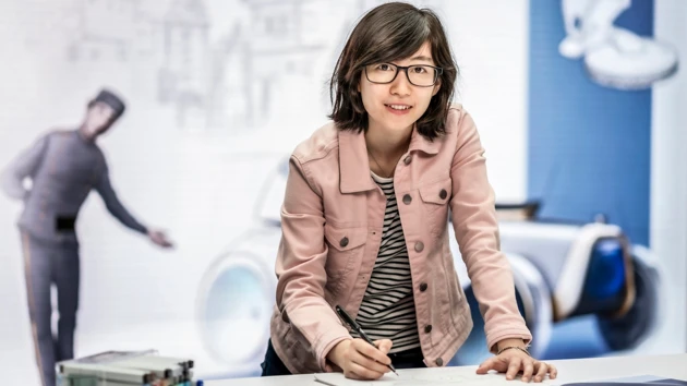 Bild på Yuhan Zhang stående vid ritbordet, i bakgrunden bild av äldre bil