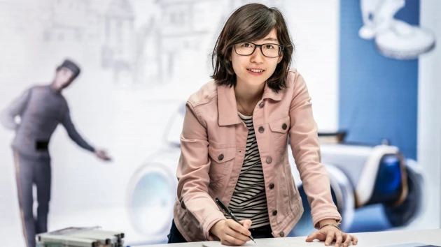 Photo of Yuhan Zhang standing at the sketch board, in the background photos of historic cars.