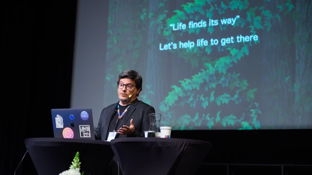 Ricard Solé, public speaker for the 15 year IceLab anniversary public lecture on terraforming ecosystems, seen here against an AI-generated backdrop depicting an arid ecosystem being transformed to a lush one thanks to synthetic organisms.