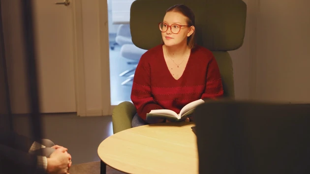 Studenten sitter i en stol och håller i en bok.