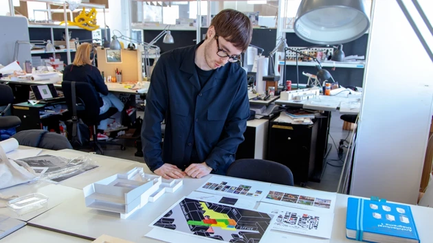 Bild på Simon From stående vid sin studentarbetsplats på Arkitekthögskolan