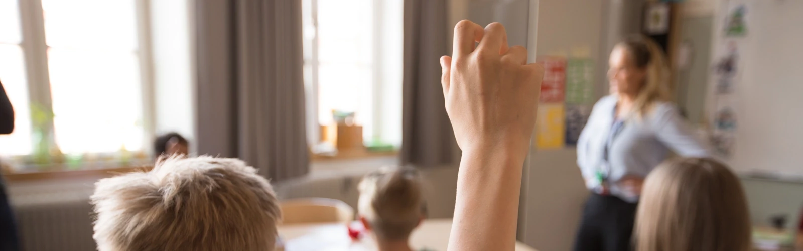 Mellanstadiebarn i klassrum. Pojke räcker upp handen.