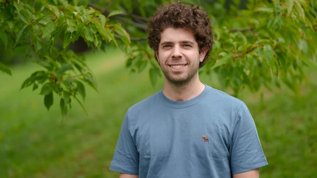 Portrait photo of Nikiforos Staveris, in the background tree branches and grass